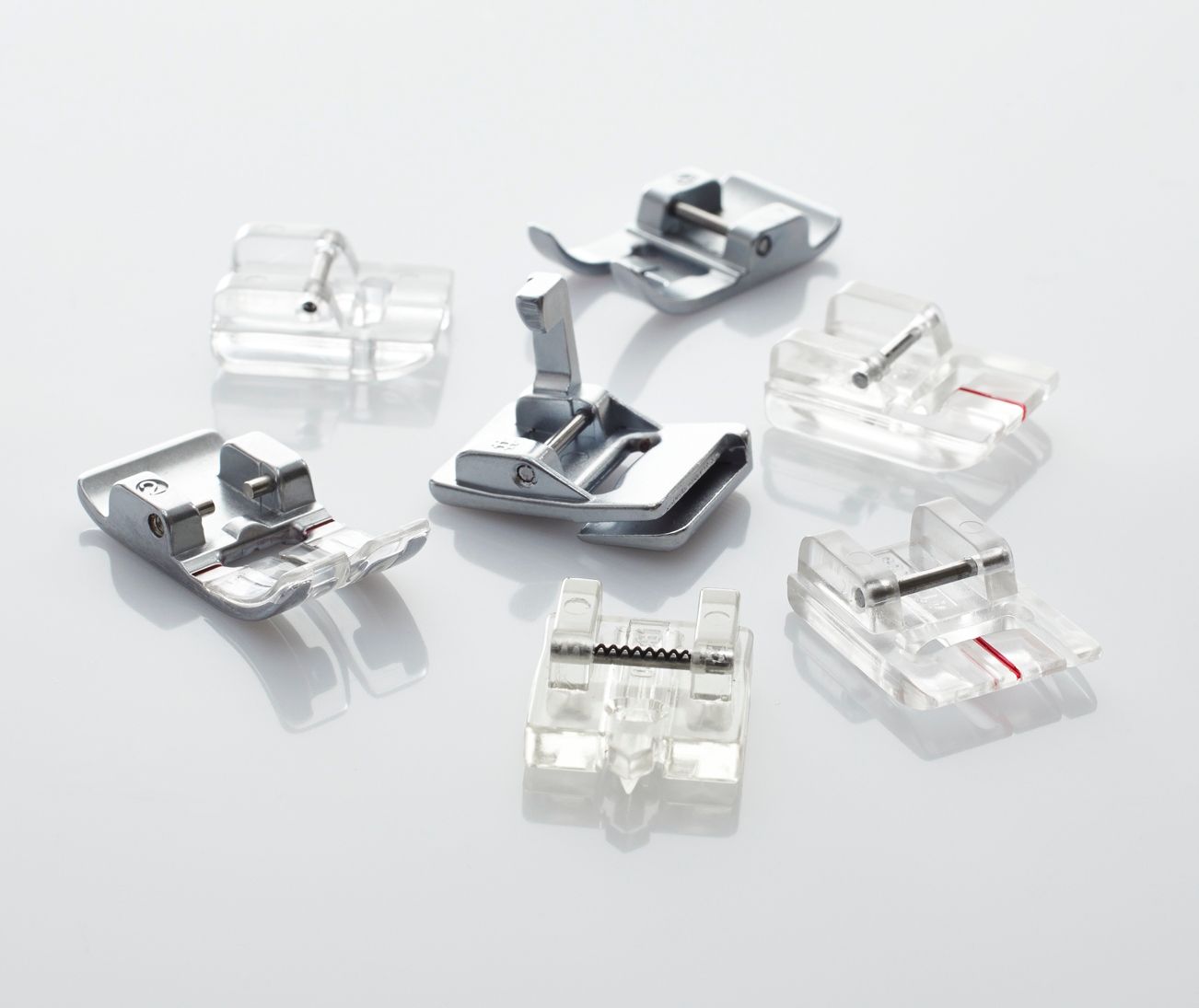 Assorted transparent and silver sewing machine presser feet arranged on a white background