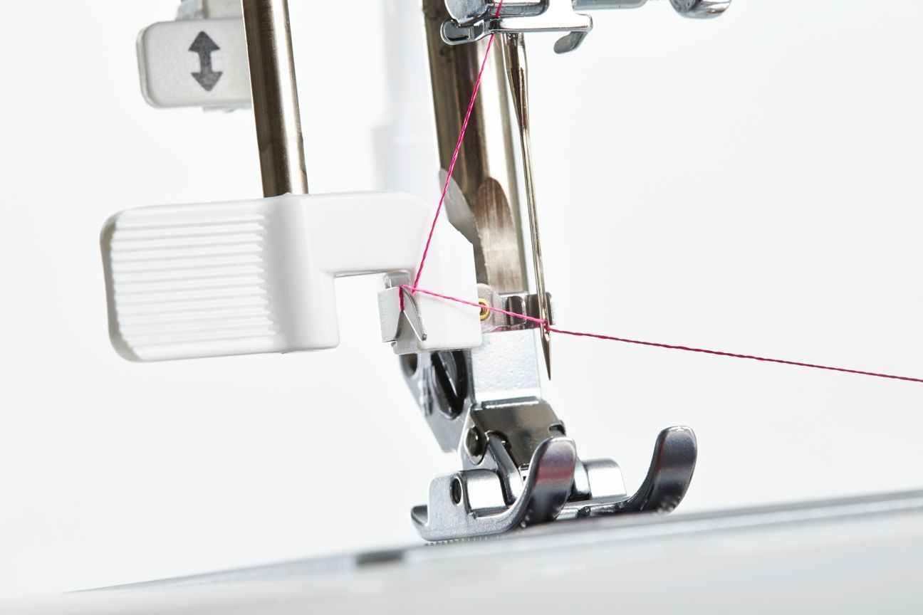 Close-up of a sewing machine presser foot stitching white fabric with red thread guide line