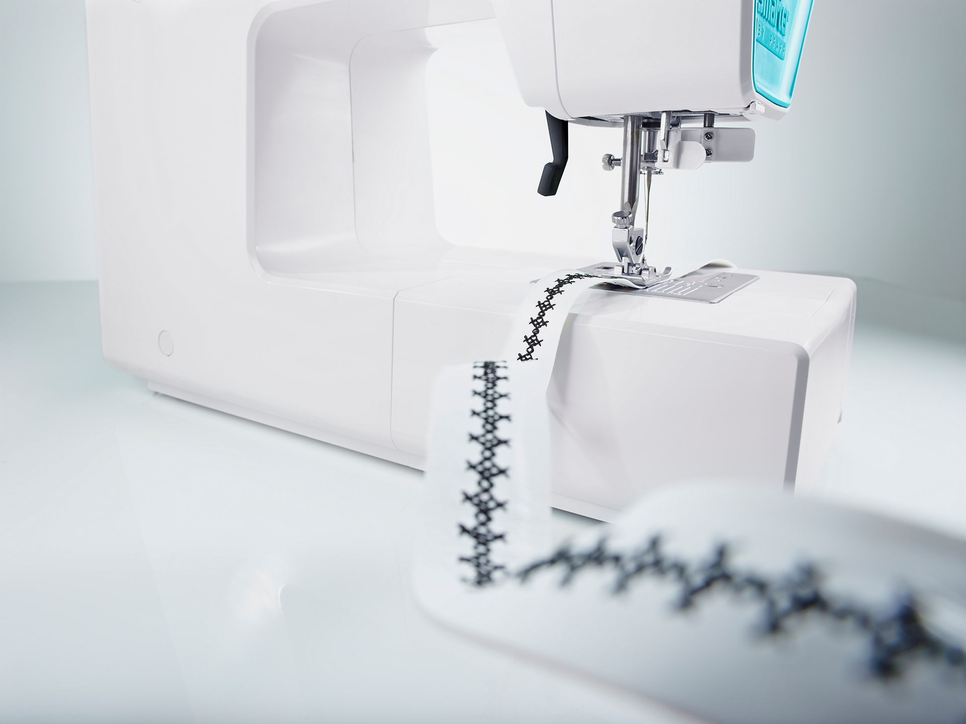 White robot arm with a coiled cable in a bright lab setting, extending over a white machine.