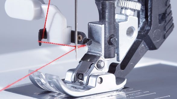 A close up of a sewing machine with a red thread coming out of it.