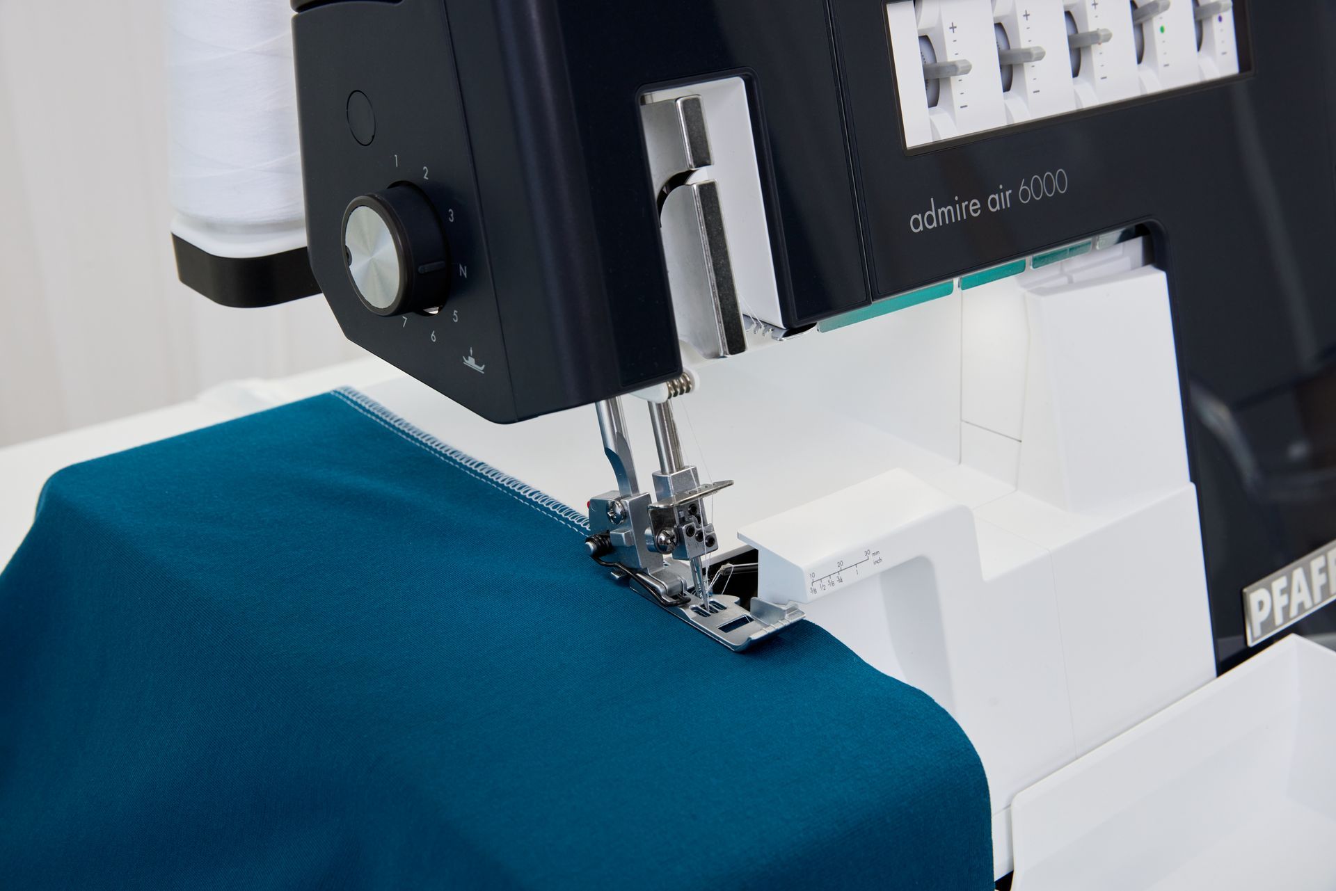 A sewing machine is stitching a piece of blue fabric.