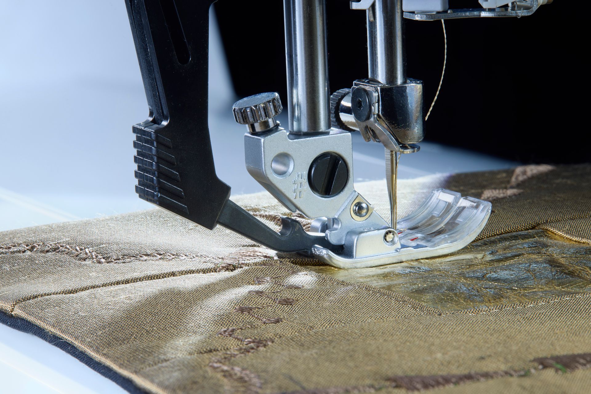Close-up of a sewing machine stitching beige fabric with a silver presser foot.