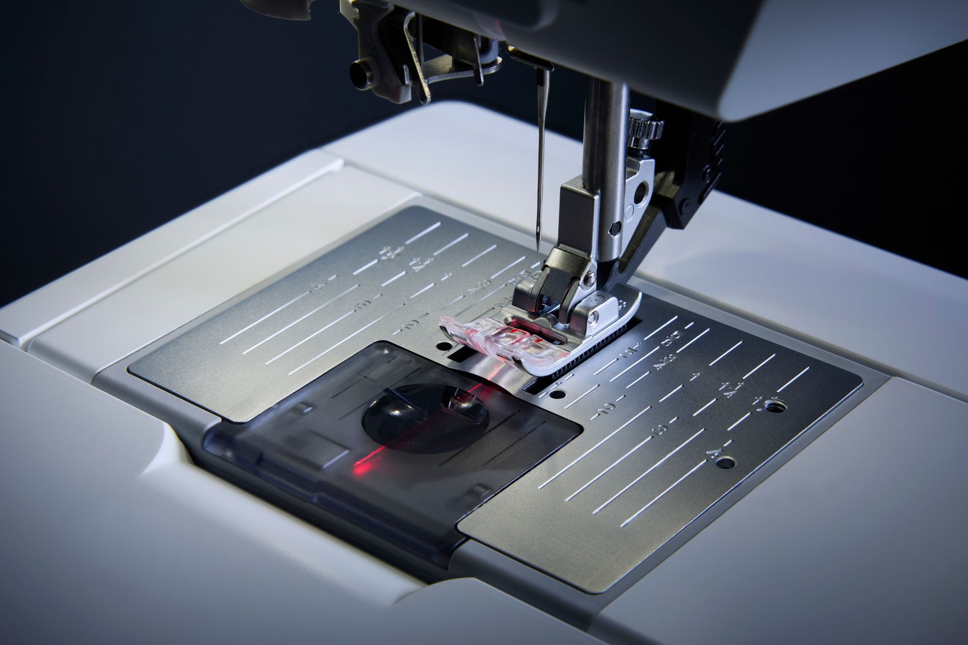 Sewing machine needle stitching black fabric on a worktable under bright light