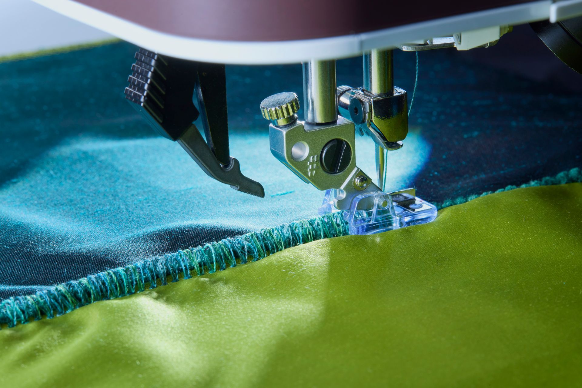 Close-up of a sewing machine stitching blue fabric onto green material