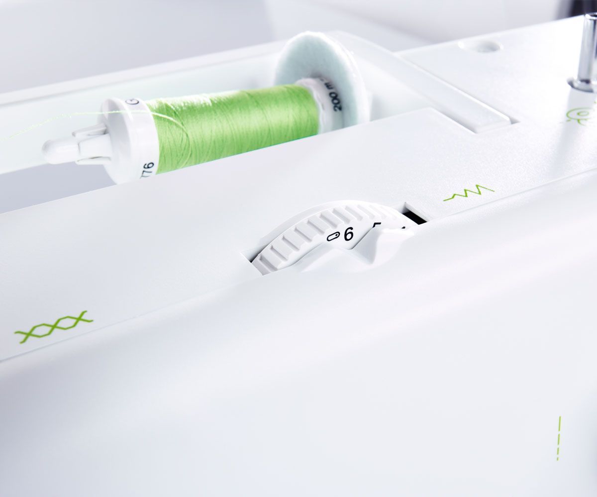 Close-up of a white sewing machine with green thread spool and stitching controls