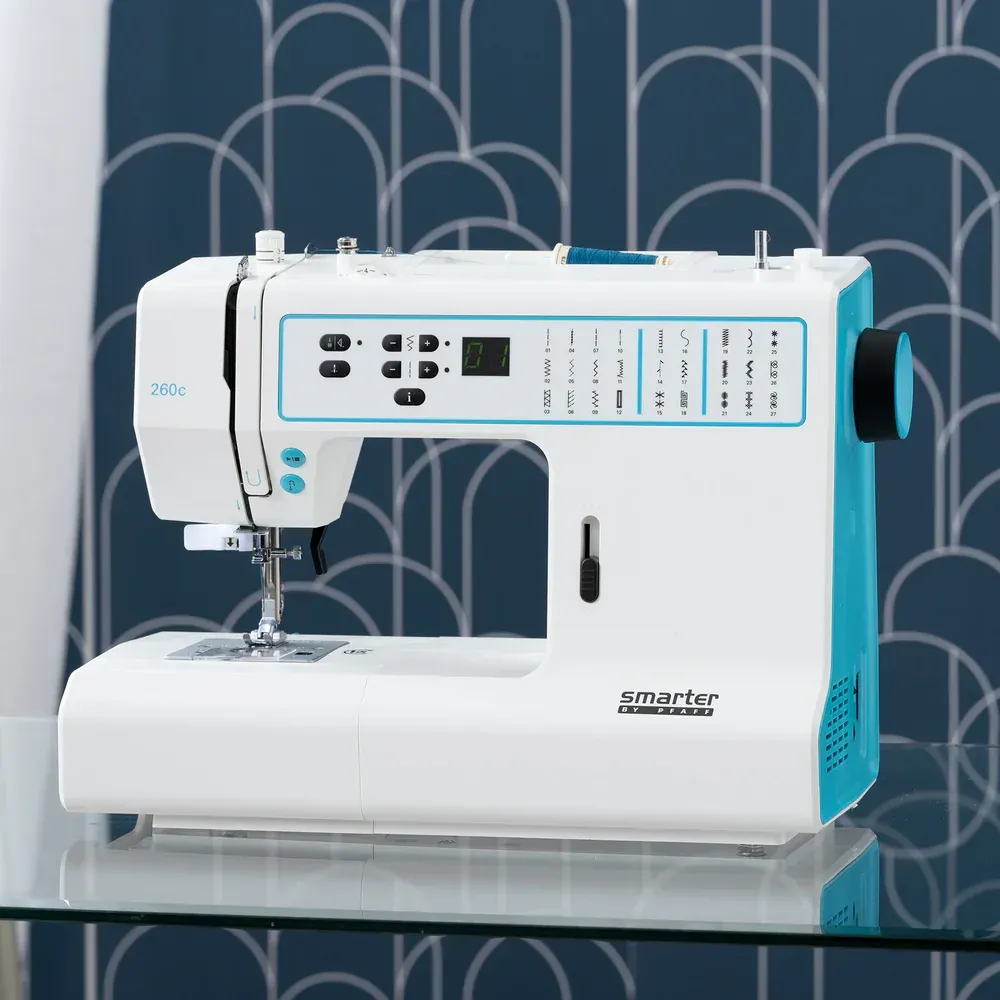 White and teal sewing machine on a reflective surface against a blue patterned background
