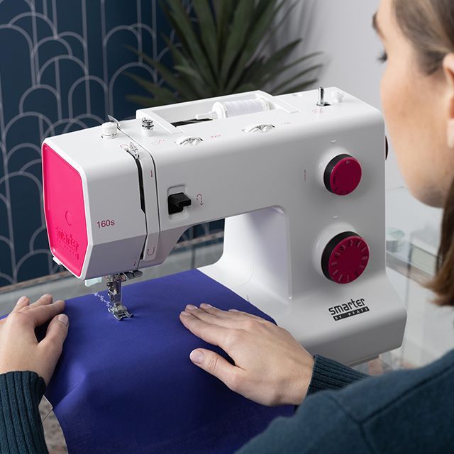 Person sewing blue fabric on a white and pink sewing machine