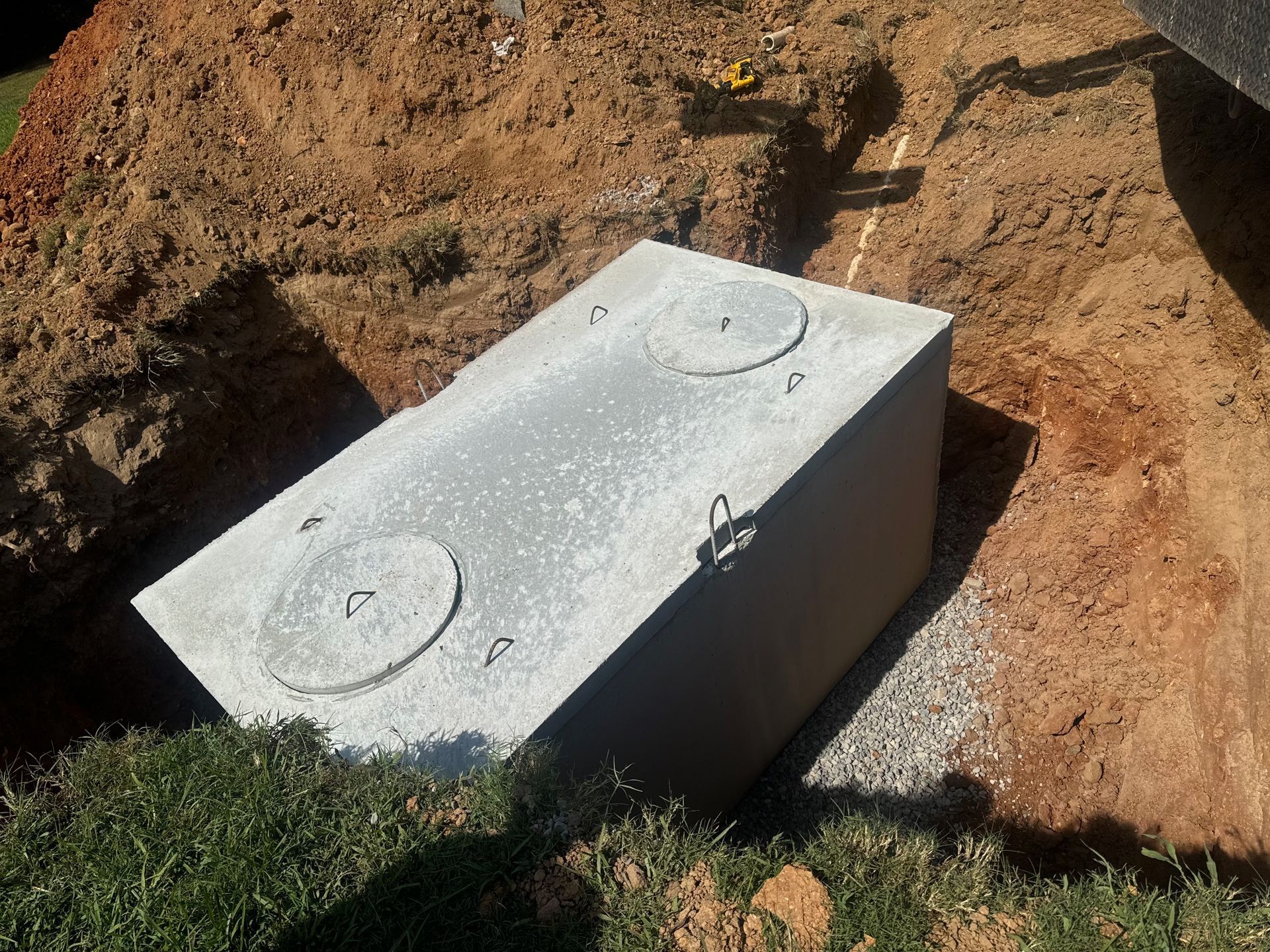 A concrete septic tank partially installed in an excavated dirt trench.