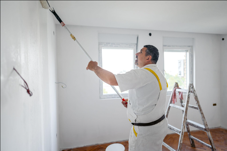 Painter applying white paint with a roller attached to an extension pole during a painting service in Moreno Valley, CA.