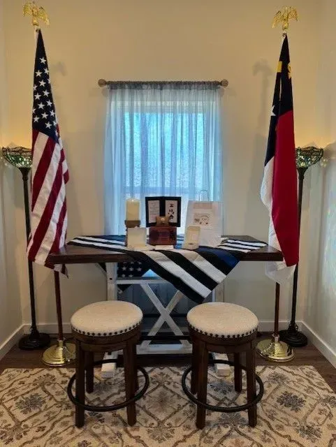 Two flags flank a table with papers and two stools in a small office-like room.