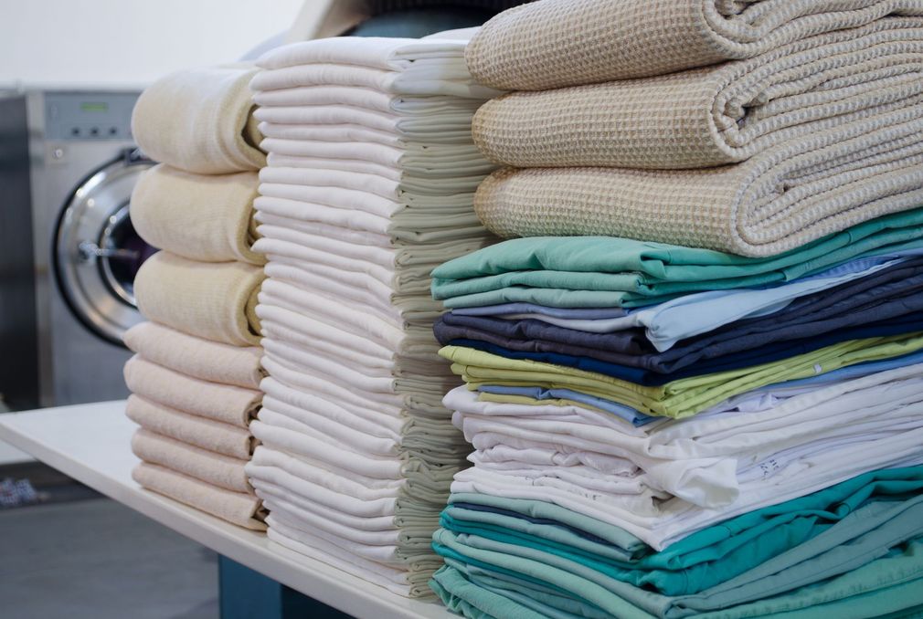 Asciugamani piegati e impilati ordinatamente, nei colori bianco, beige e verde acqua, accanto a una lavatrice.