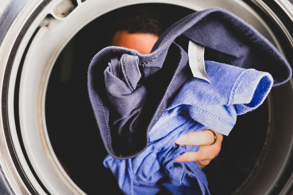 Persona che tiene una pila di biancheria all'interno del cestello di una lavatrice