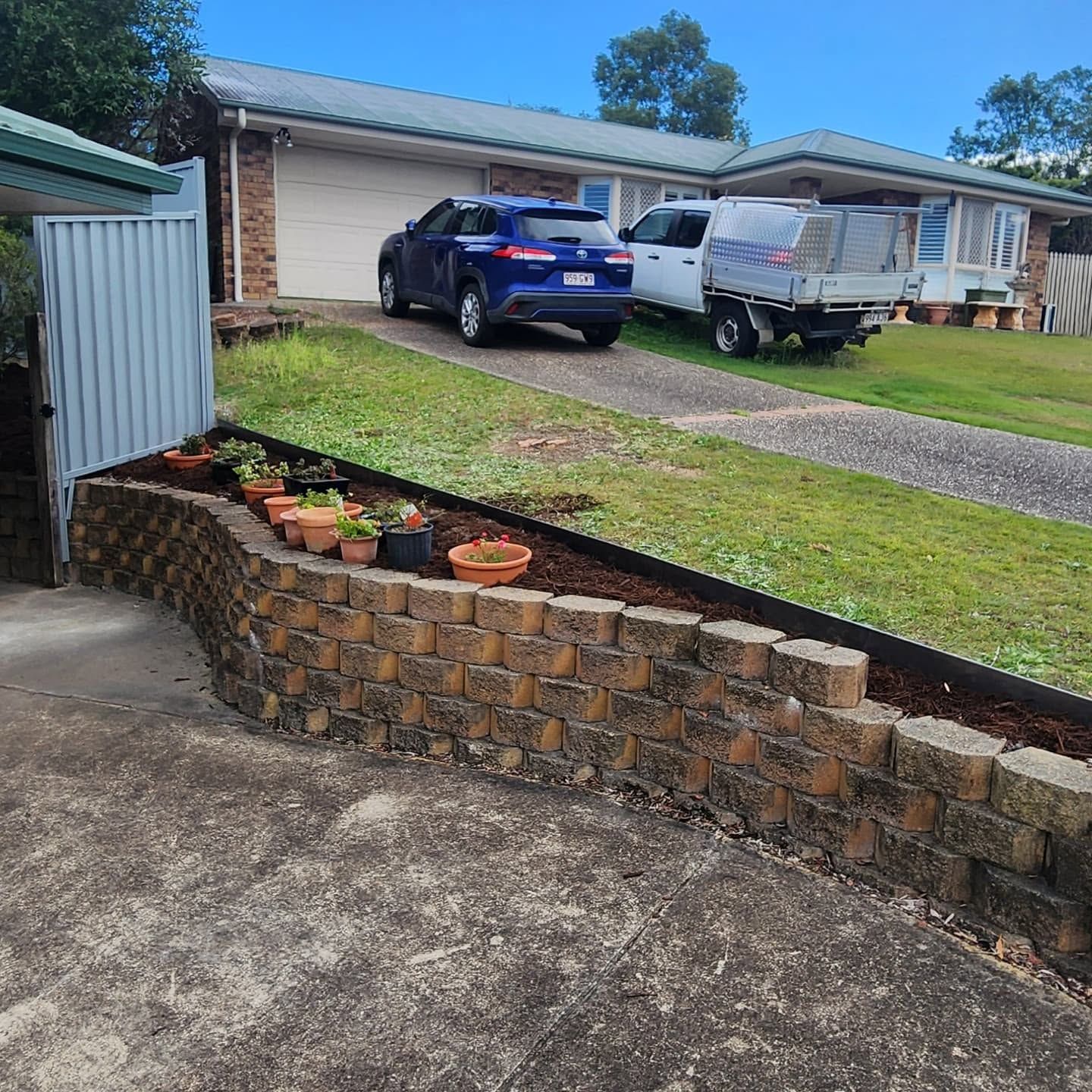 Front yard with brick planter, parked blue SUV and white van, and a house in the background.
