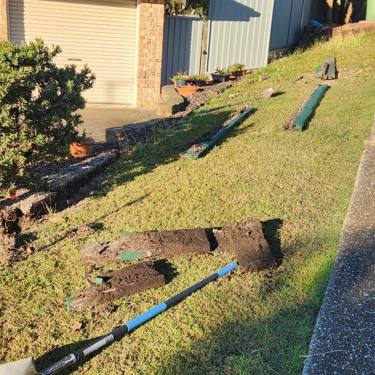 Broken wooden fence posts and debris on a grassy slope beside a house and driveway.