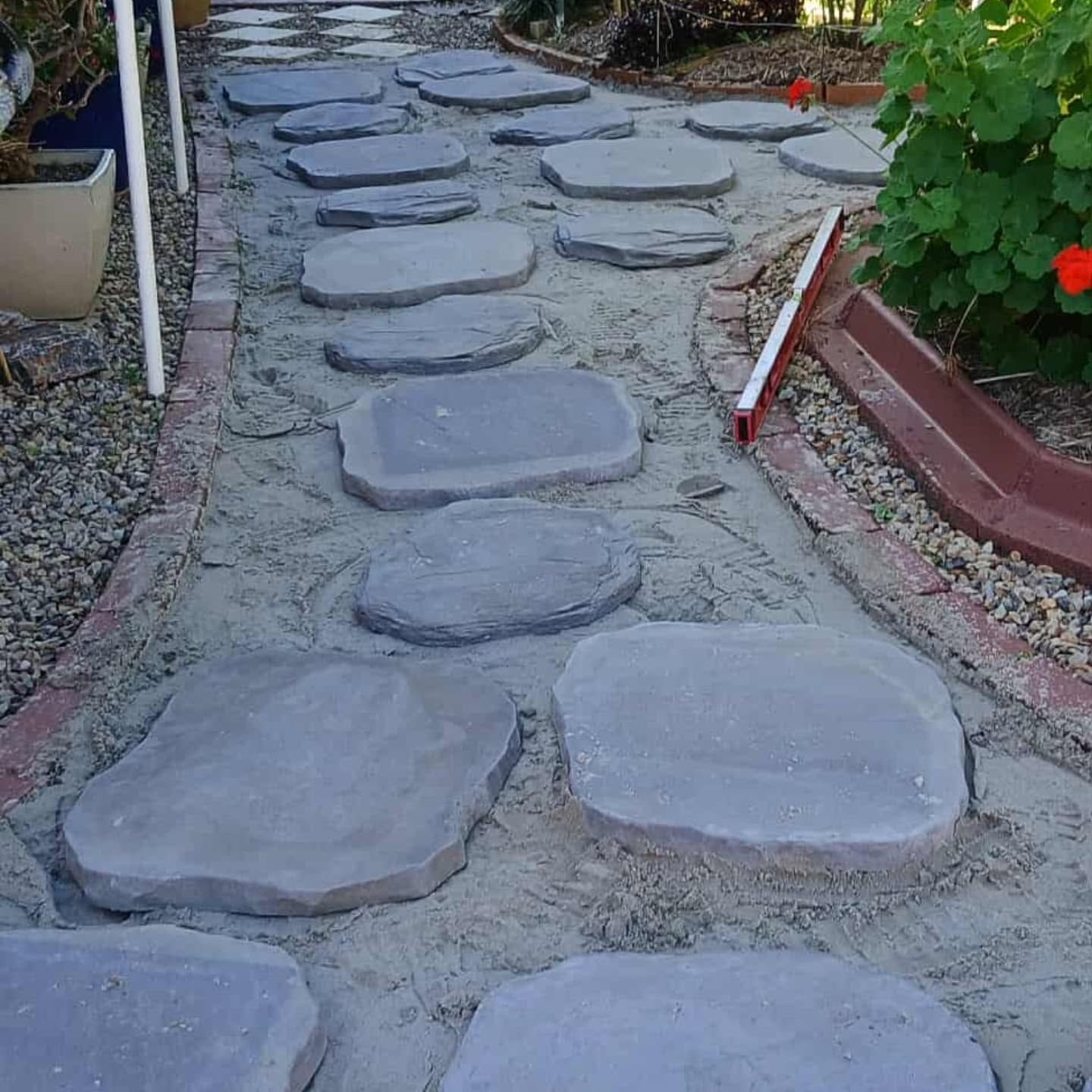 Stepping-stone garden path with flat gray pavers bordered by plants and red edging