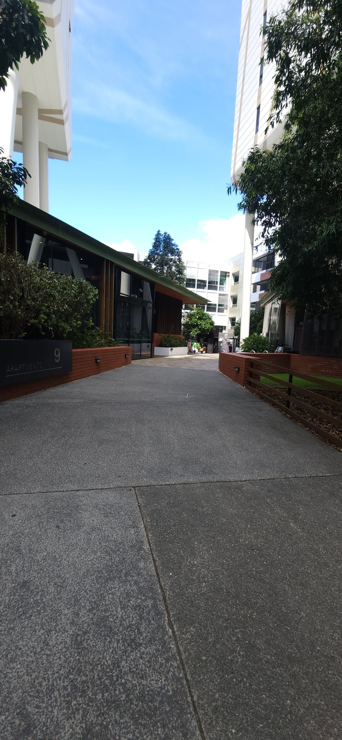 Courtyard walkway between buildings with trees, brick planters, and a blue sky above