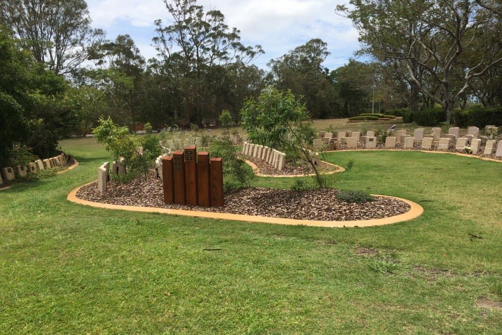Circular outdoor sculpture with brown posts, surrounded by grass and trees