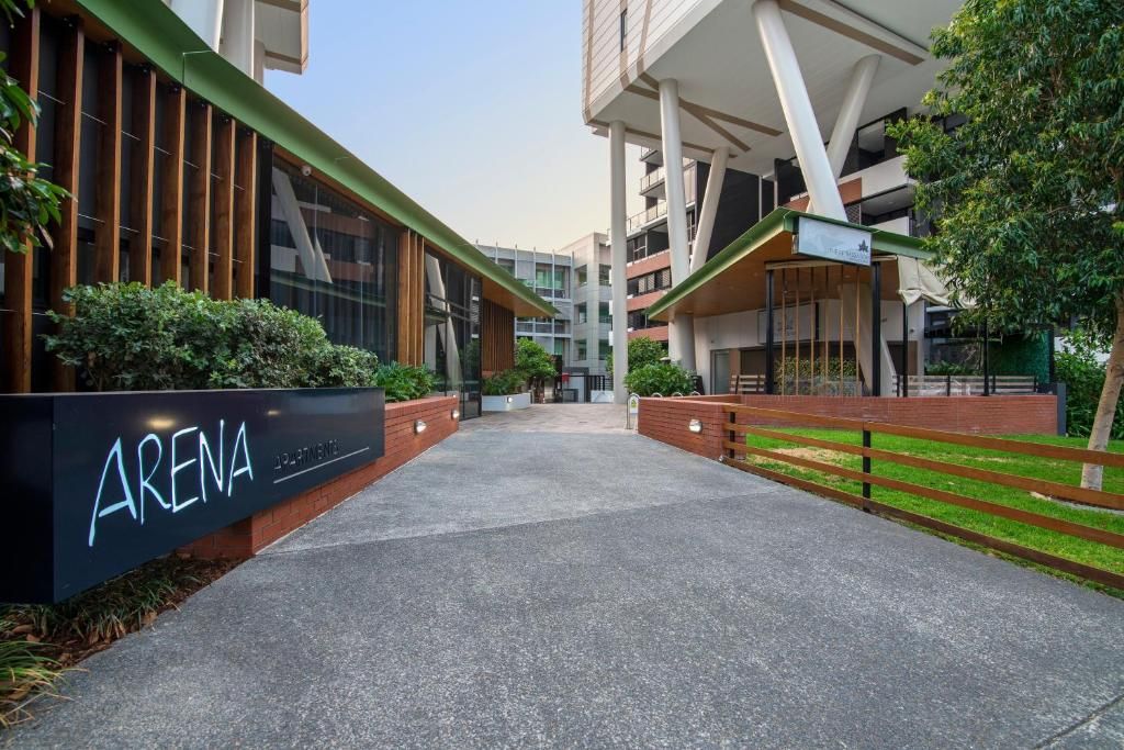 Walkway beside a modern building and arena sign, with brick planters and trees