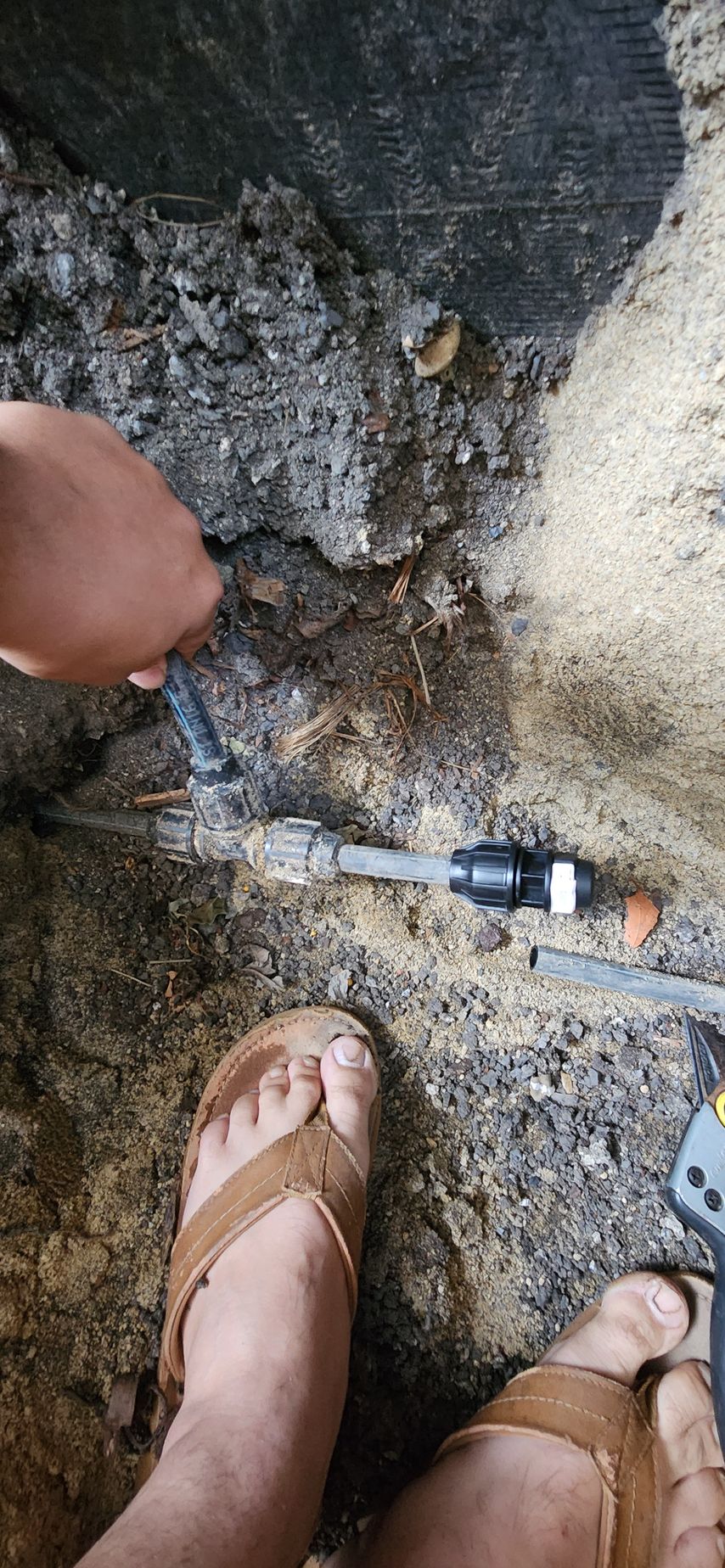 Foot and hand inspecting a muddy floor crack with a small pipe fitting.