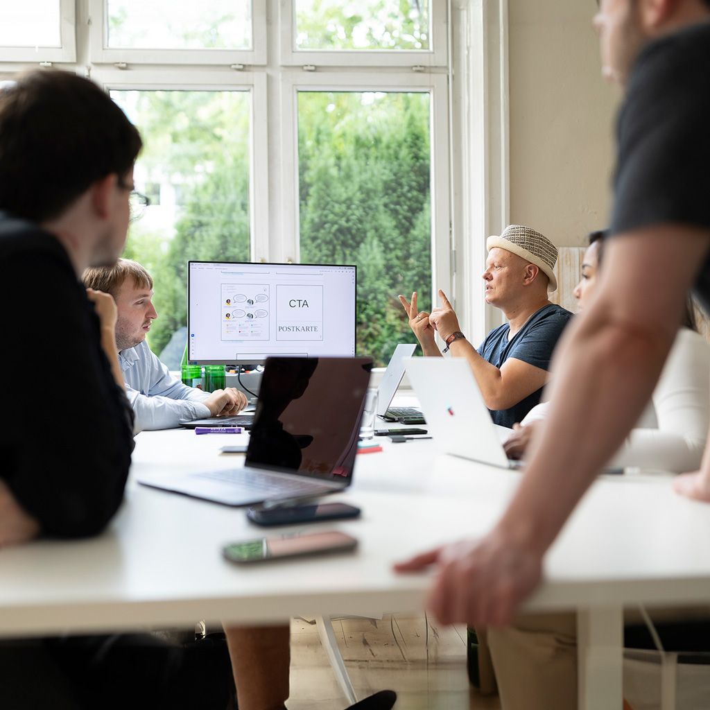 Teambesprechung an einem weißen Tisch mit Laptops und einer Präsentation auf einem Monitor in einem hellen Büro