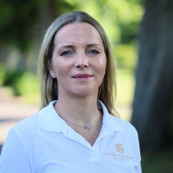 Frau trägt ein weißes Poloshirt mit Logo, im Freien, blickt in die Kamera.