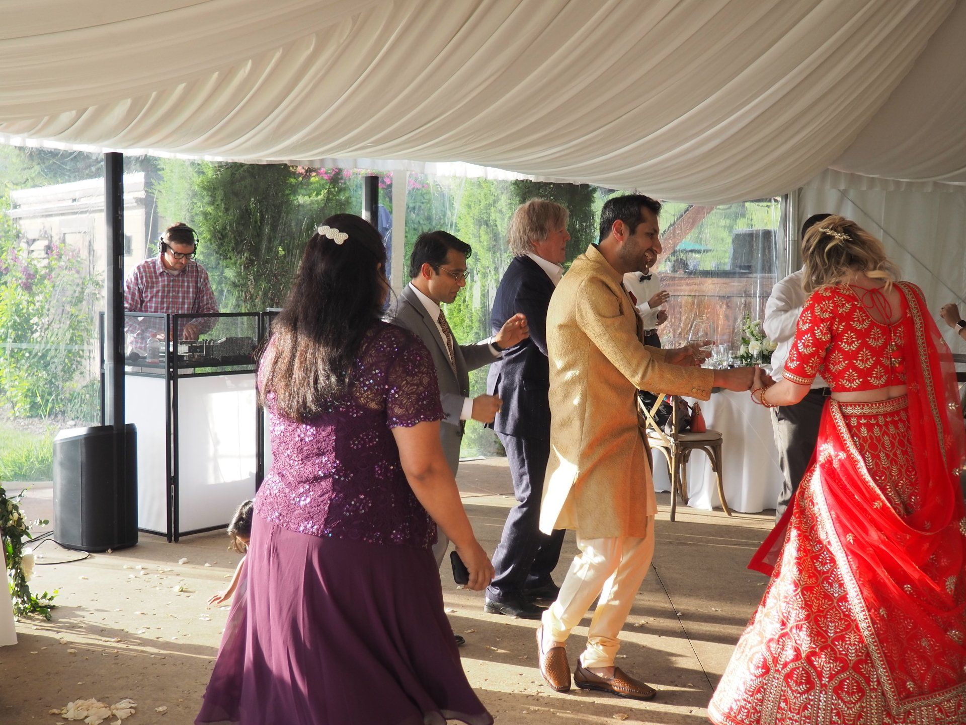 A group of people are dancing in a tent at a wedding reception.