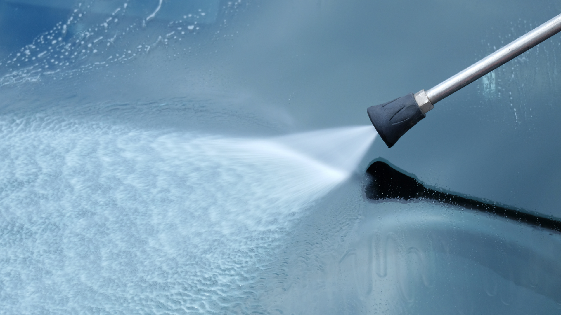 Pressure washer spraying water across a car windshield during cleaning