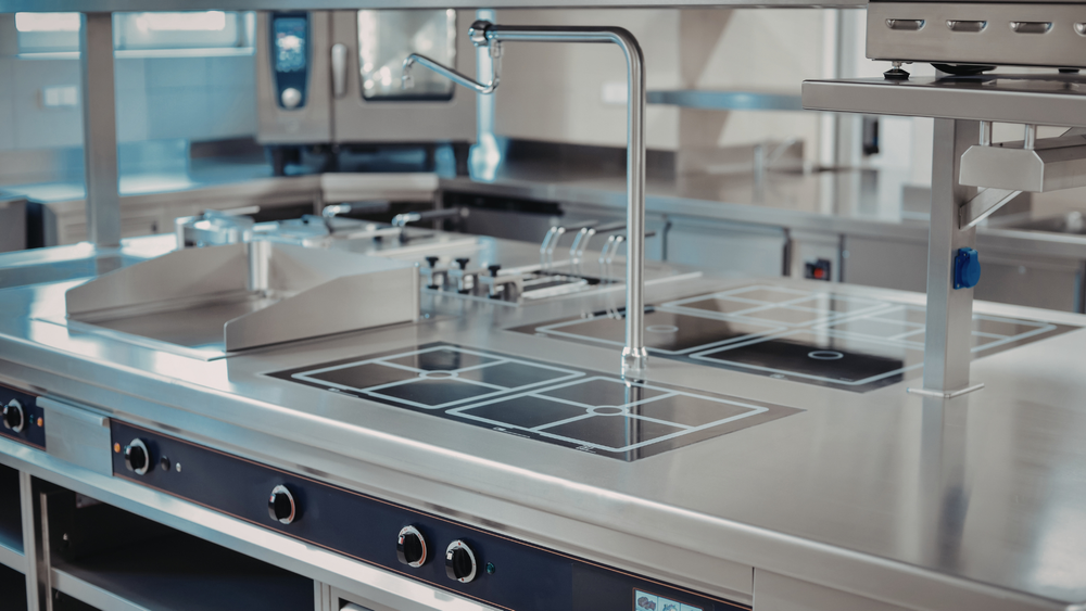 Stainless steel commercial kitchen sink with faucet and drainboard in a clean industrial workspace