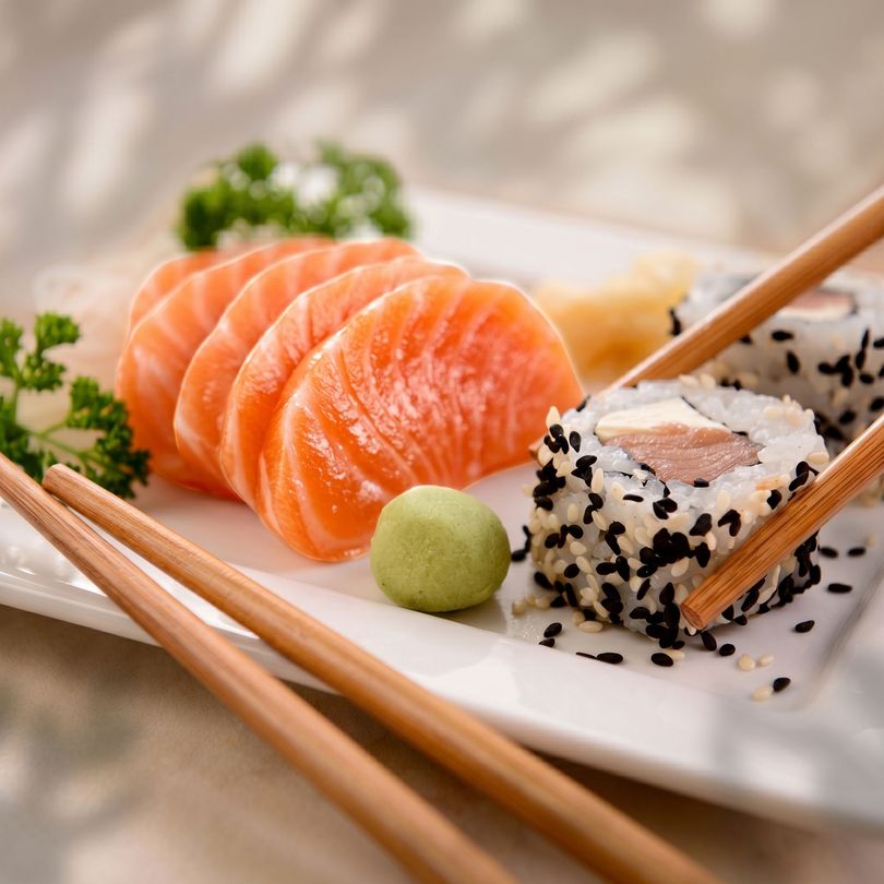 Sushi platter with salmon nigiri, sesame-coated roll, chopsticks, and wasabi on a white plate