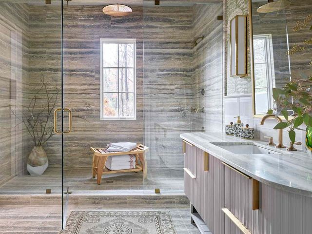 AD Construction NJ - Luxurious bathroom with stone walls, glass shower, wooden bench, and marble countertop.