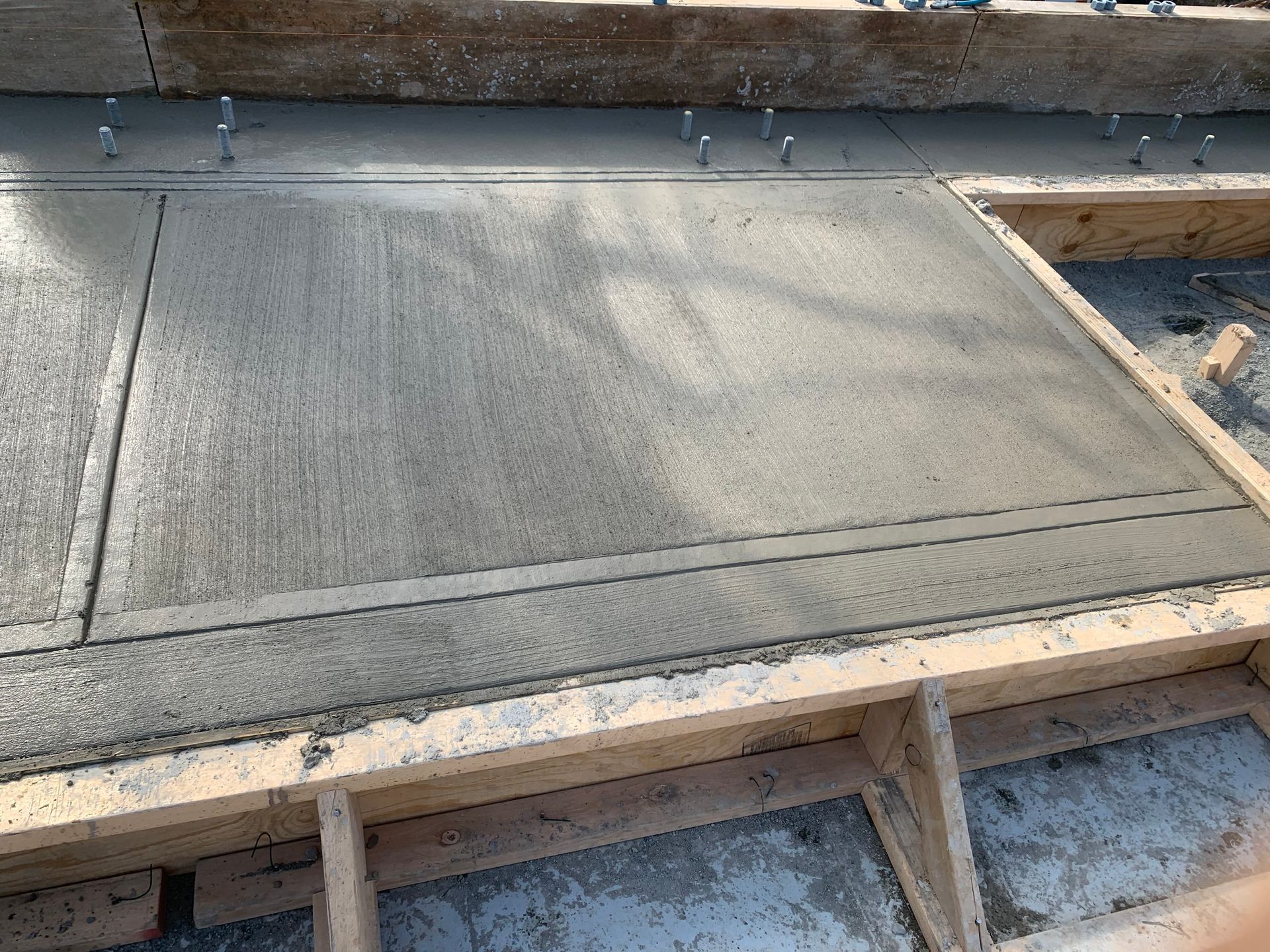 AD Construction NJ - Freshly poured concrete within wooden forms, with metal pins protruding.