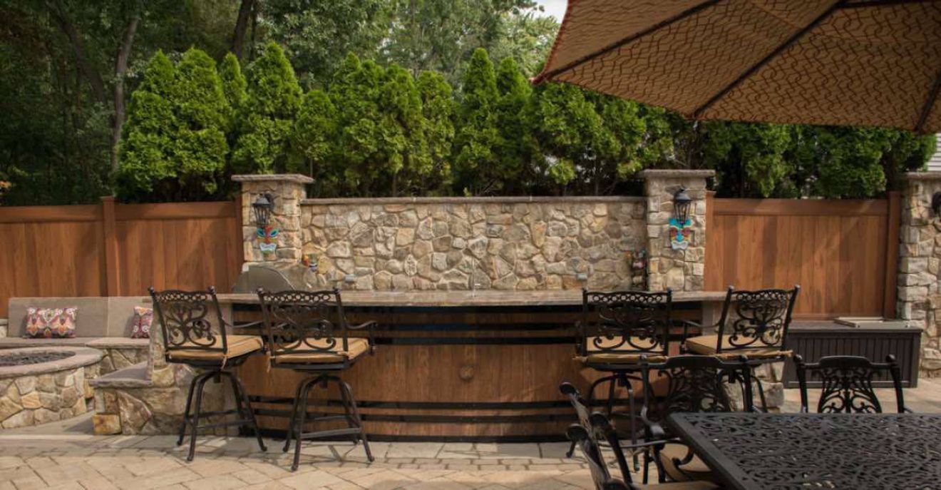 AD Construction NJ - Outdoor bar with stone facade, wooden accents, and wrought iron bar stools.