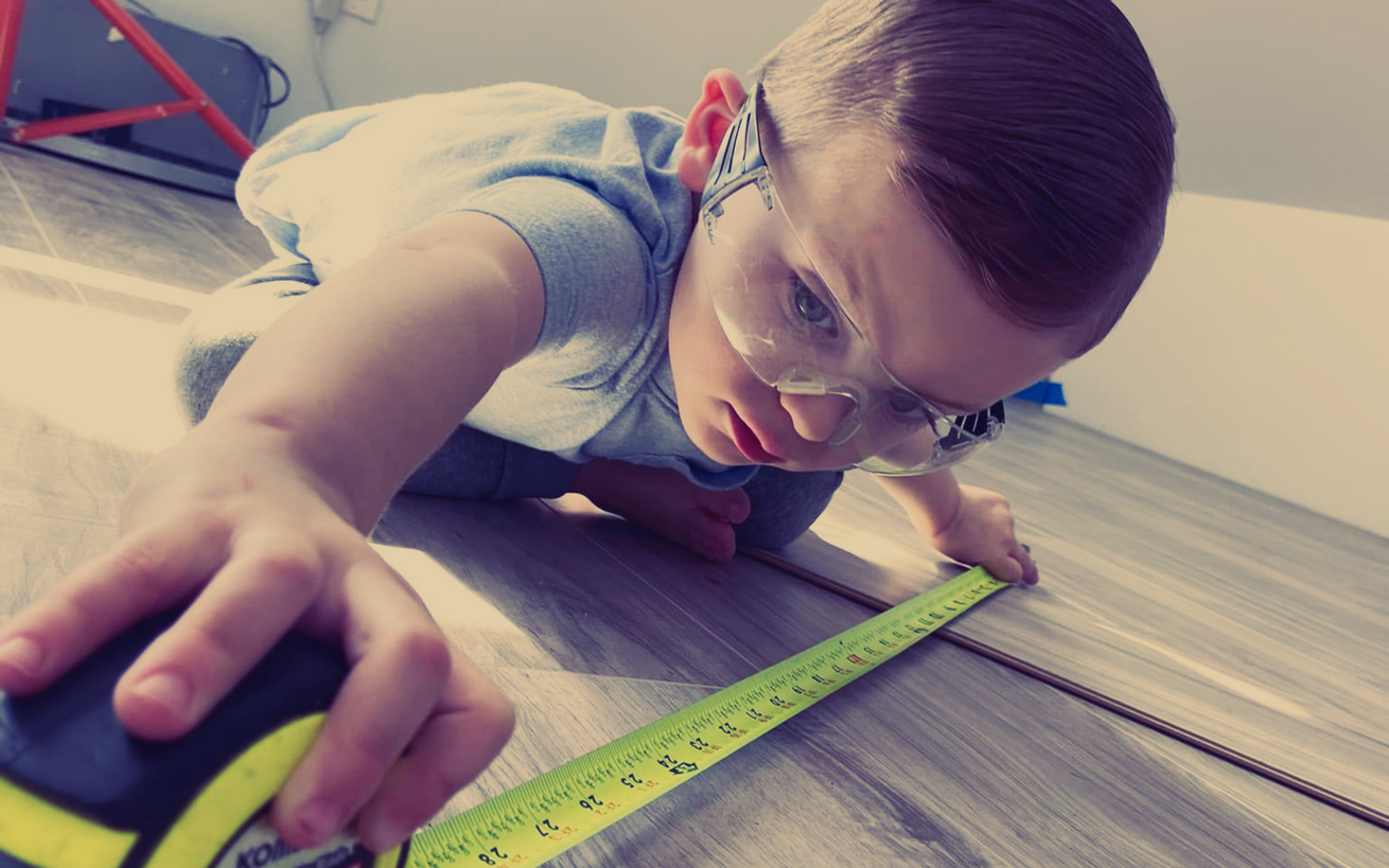 AD Construction NJ - Boy wearing safety glasses measures wood flooring with a tape measure.