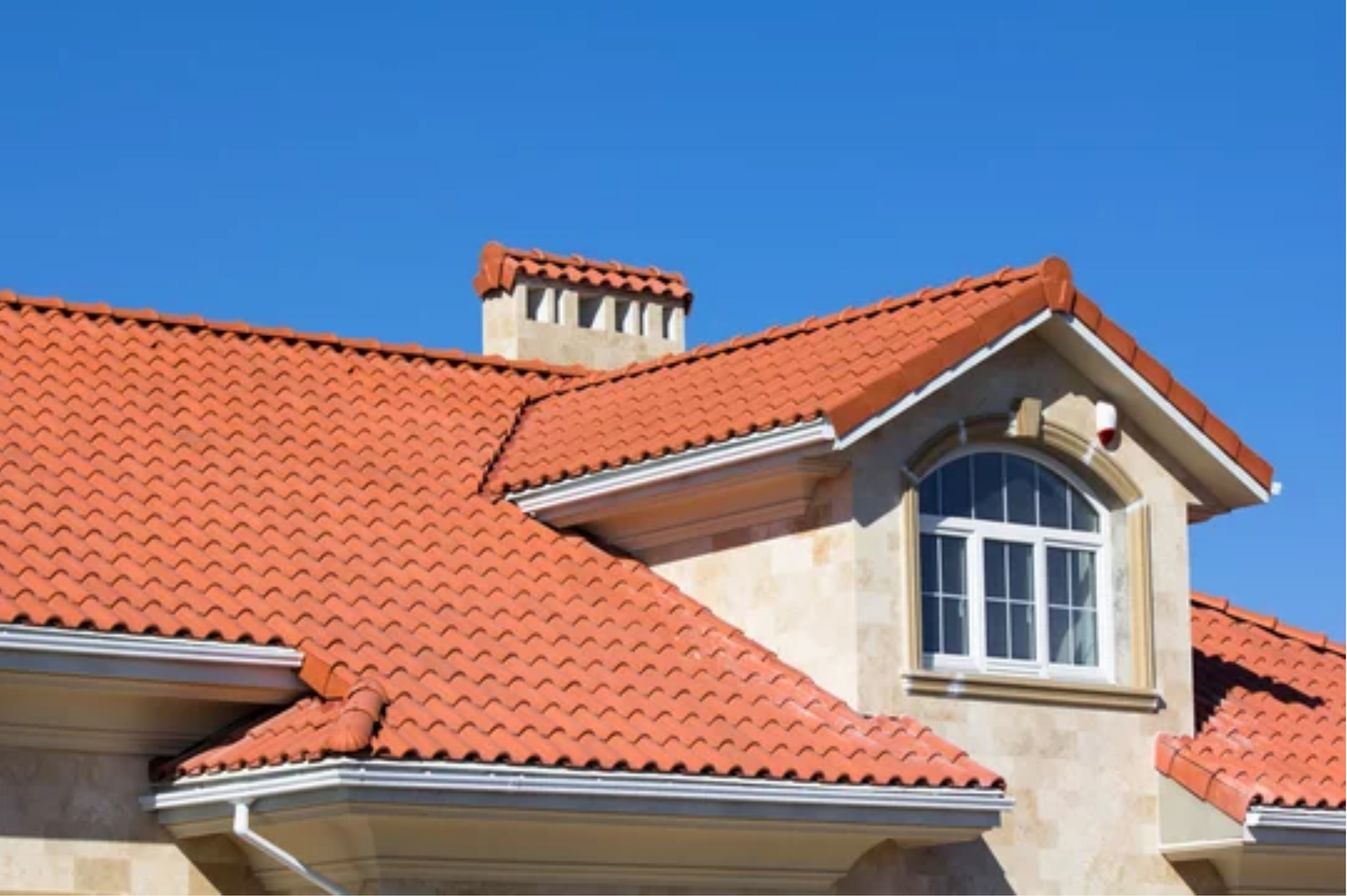 AD Construction NJ - Orange tile roof on a beige house with a chimney and a dormer window against a blue sky.