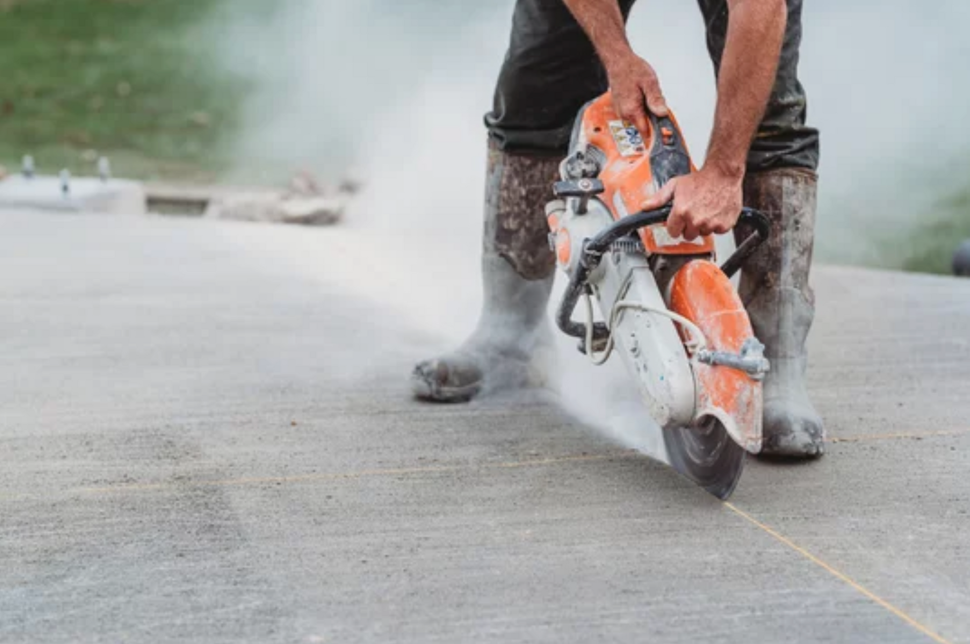 AD Construction NJ - Person cutting concrete with a saw, creating dust. Gray concrete, orange saw, water.