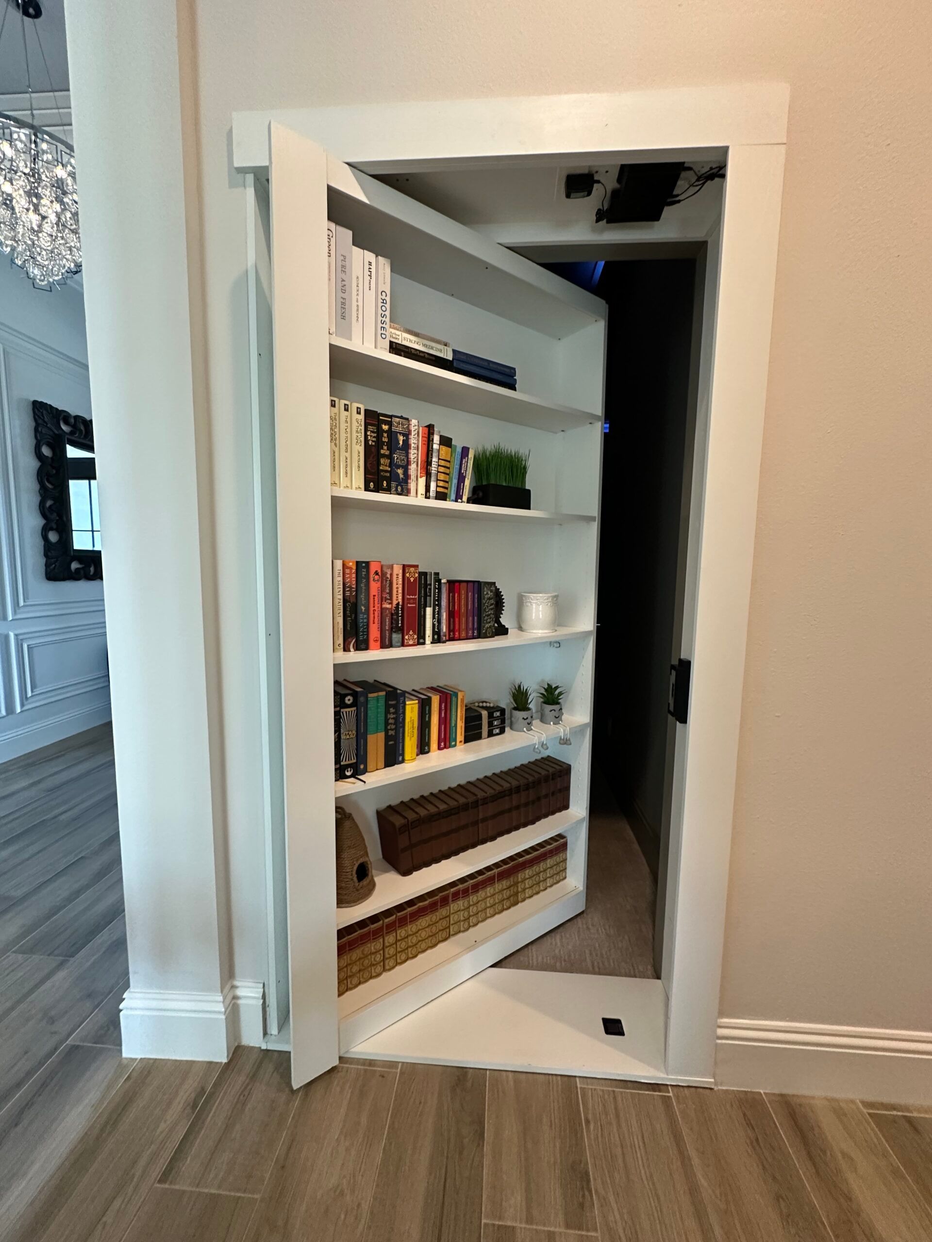 AD Construction NJ - White bookshelf door, open to reveal a dark, hidden room. Books and decorative items line the shelves.