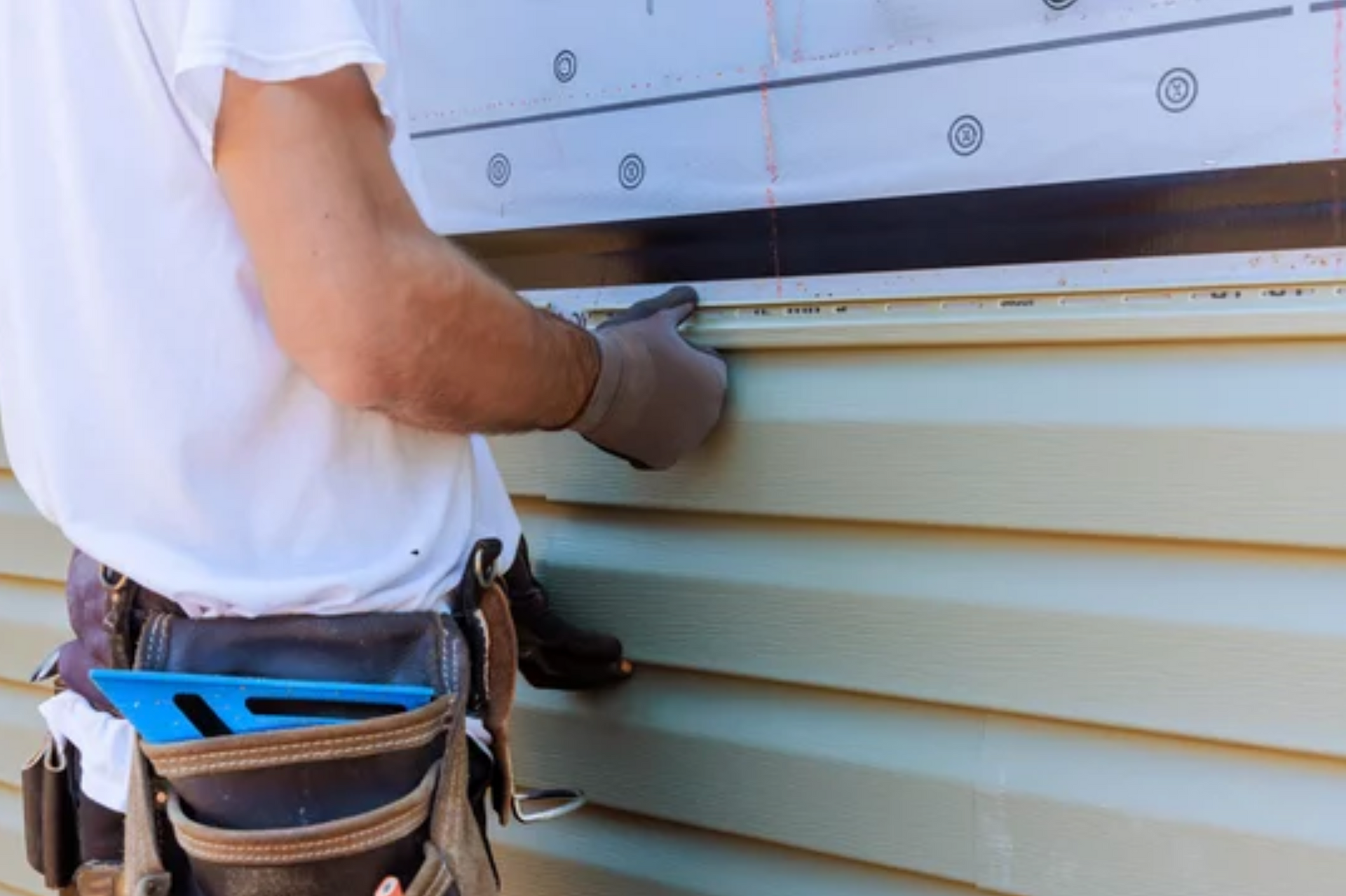 AD Construction NJ - A person installing light green vinyl siding on a building, wearing work gloves and a tool belt.
