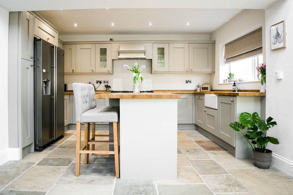 AD Construction NJ - Kitchen with gray cabinets, island with wooden countertop, and a potted plant on the stone tile floor.