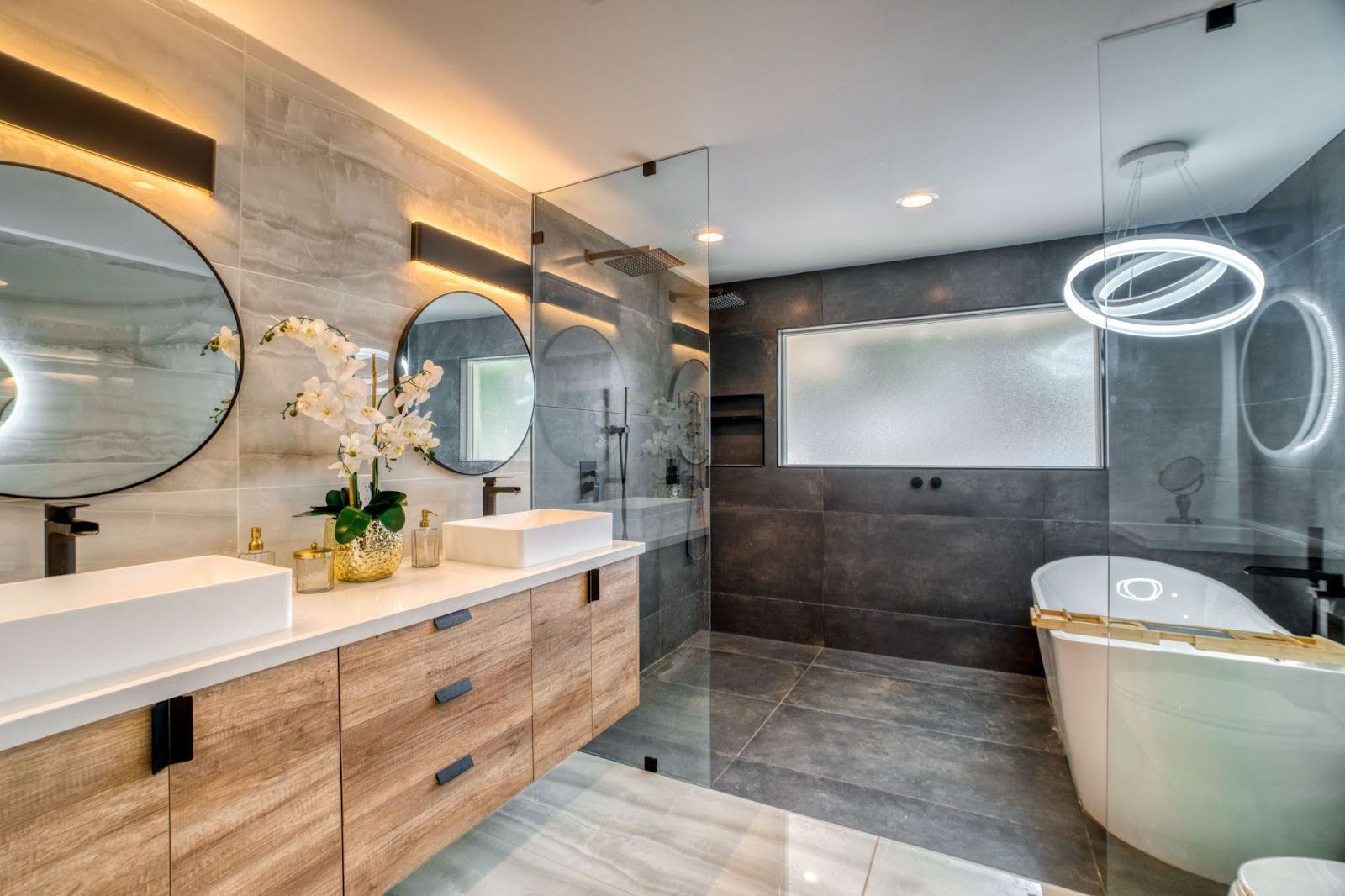 AD Construction NJ - Modern bathroom with gray tile, wooden vanity, glass shower, and freestanding tub.