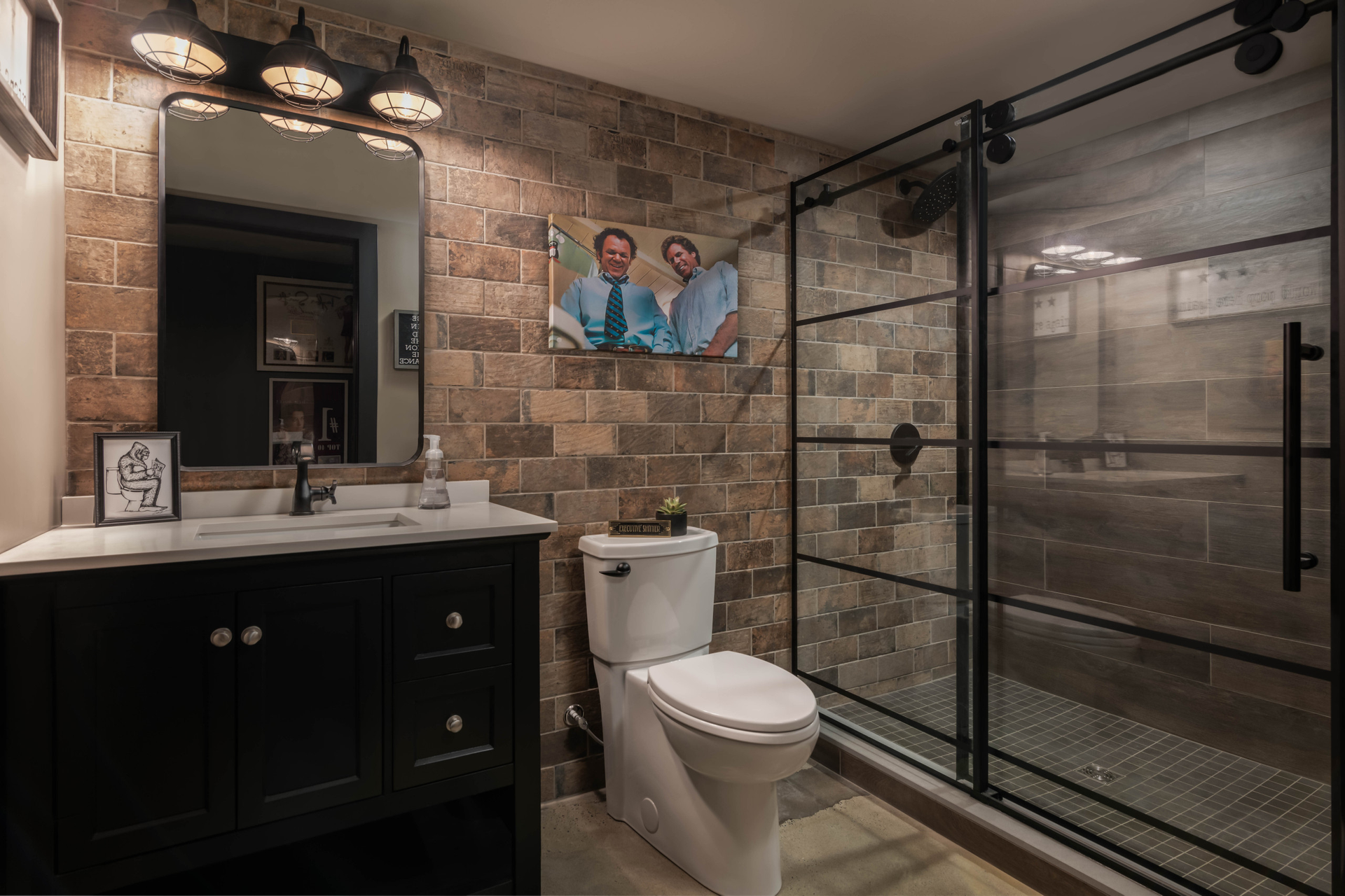 AD Construction NJ - Bathroom with brick accent wall, black vanity, toilet, and a glass-enclosed shower.