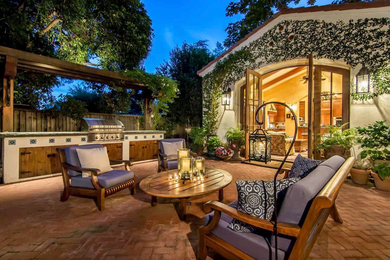 AD Construction NJ - Backyard patio with outdoor kitchen, seating, and open doors to a room, illuminated at dusk.