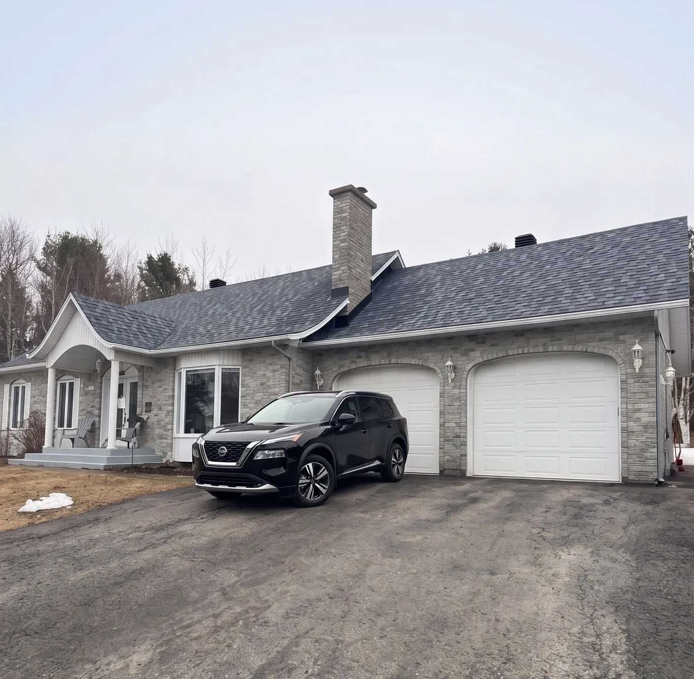 Un VUS noir gar&eacute; devant une maison moderne en pierre avec garage double et toit ardois&eacute;.