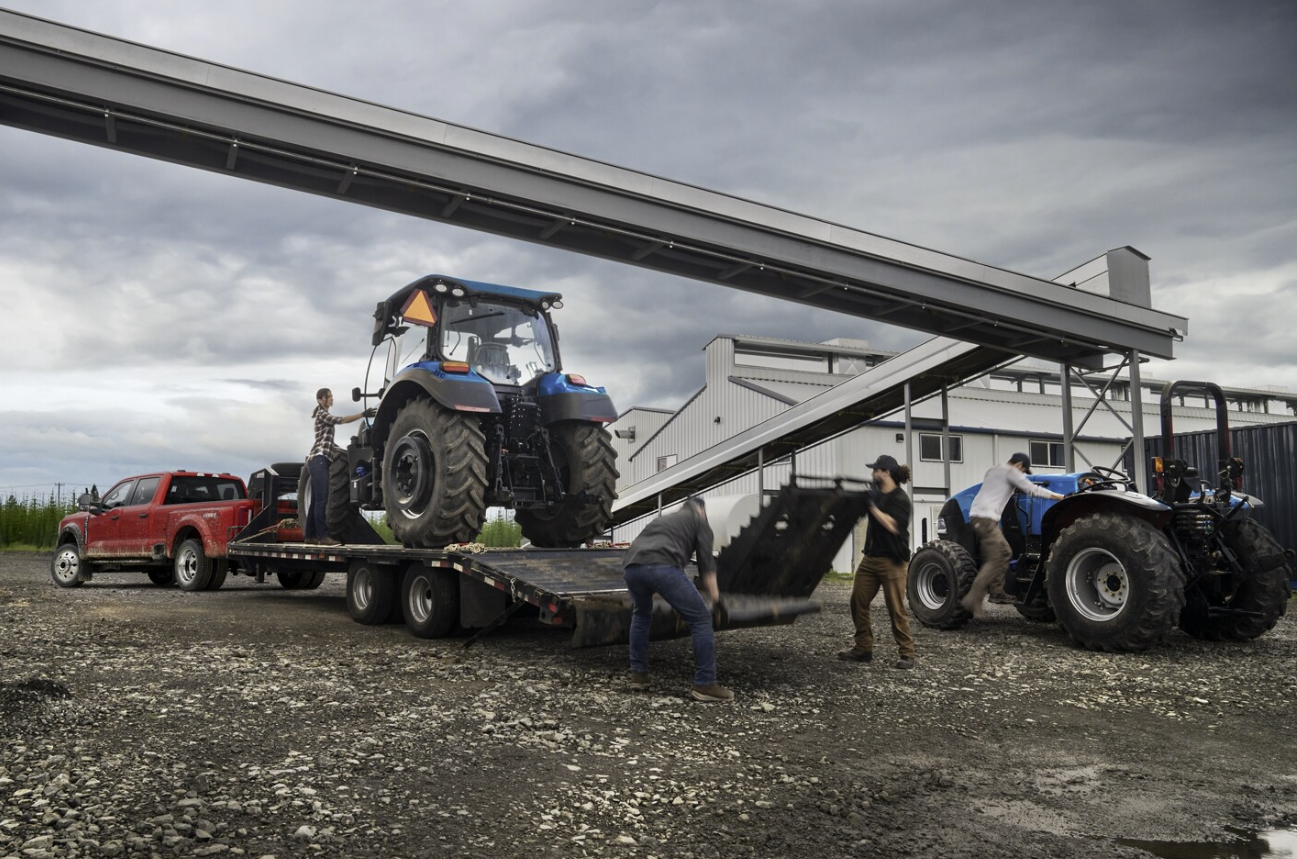A red truck is towing a blue tractor on a flatbed trailer.