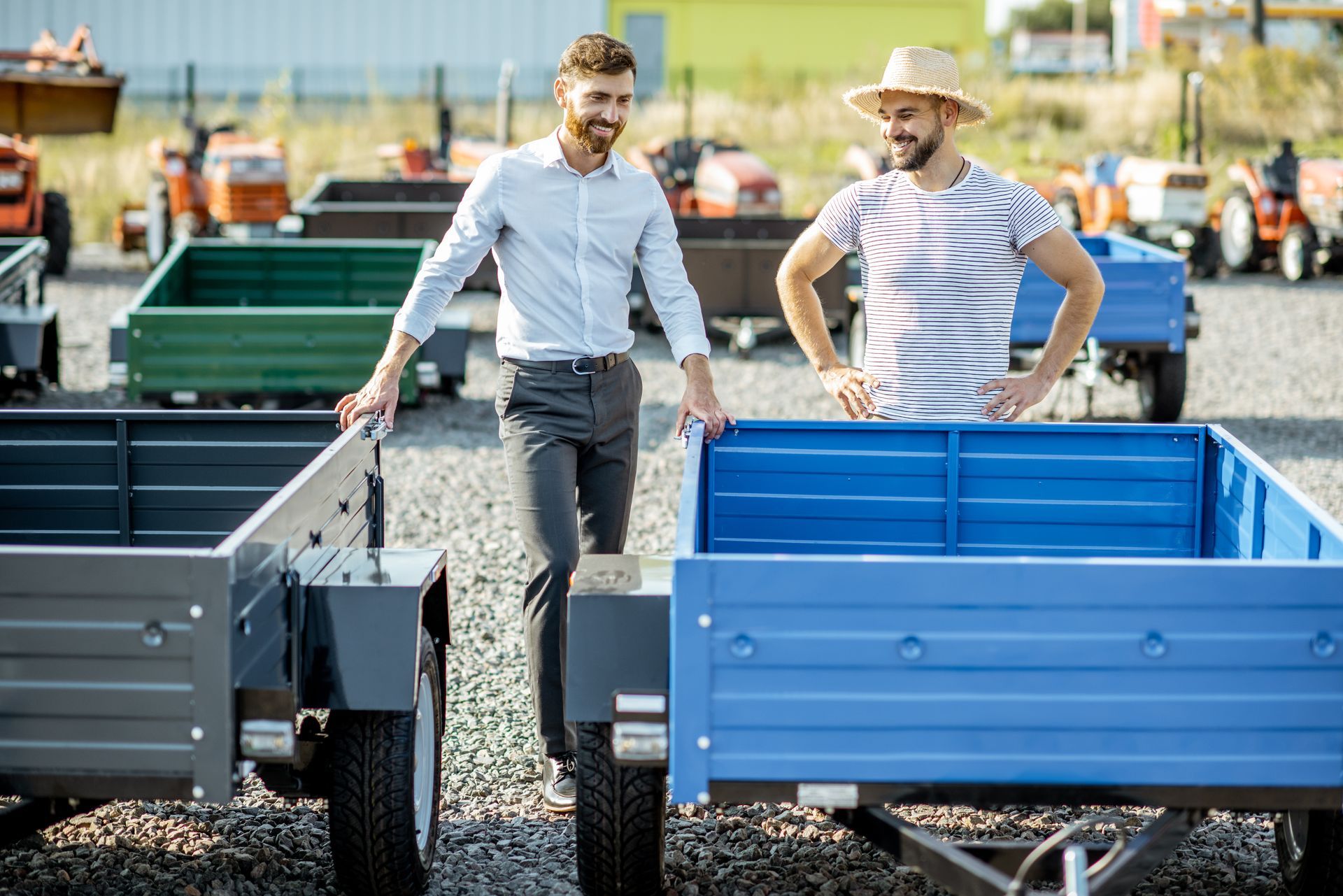 Two men are standing next to each other looking at trailers in a showroom.