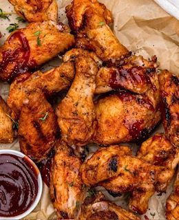 Pile of golden, crispy chicken wings, sprinkled with herbs and cheese, in a basket.