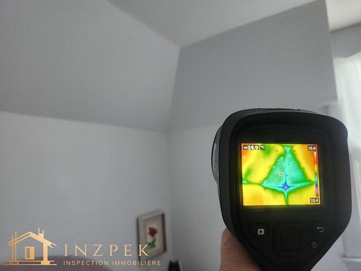 Une caméra infrarouge scanne un plafond blanc, révélant une perte de chaleur sous forme de zones plus froides (bleu).
