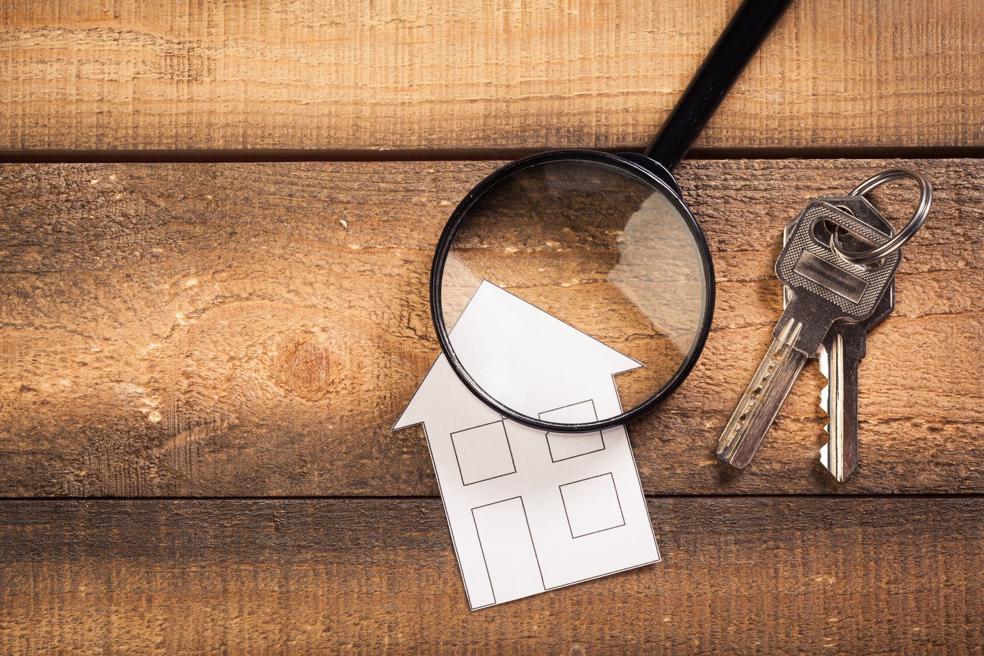 Loupe sur une maison en papier avec des clés sur une surface en bois, suggérant une inspection de la maison.
