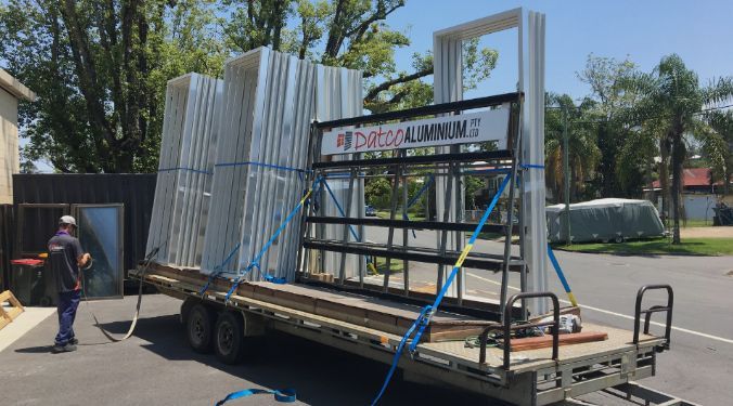 A Man Is Standing Next To A Trailer With A Stack Of Aluminum Frames On It — Datco Aluminium Pty Ltd In Murwillumbah, NSW