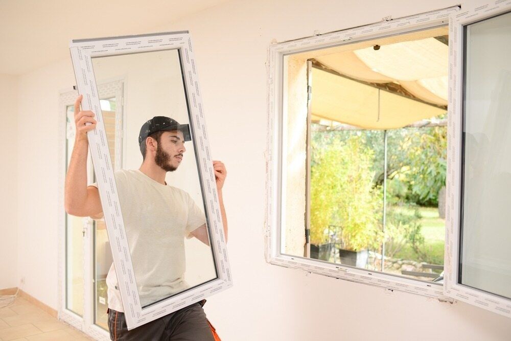 A Man Is Holding A Window Frame In A Room — Datco Aluminium Pty Ltd In Murwillumbah, NSW