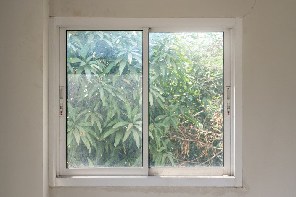 A Sliding Glass Window With A View Of Trees In A Room — Datco Aluminium Pty Ltd In Murwillumbah, NSW